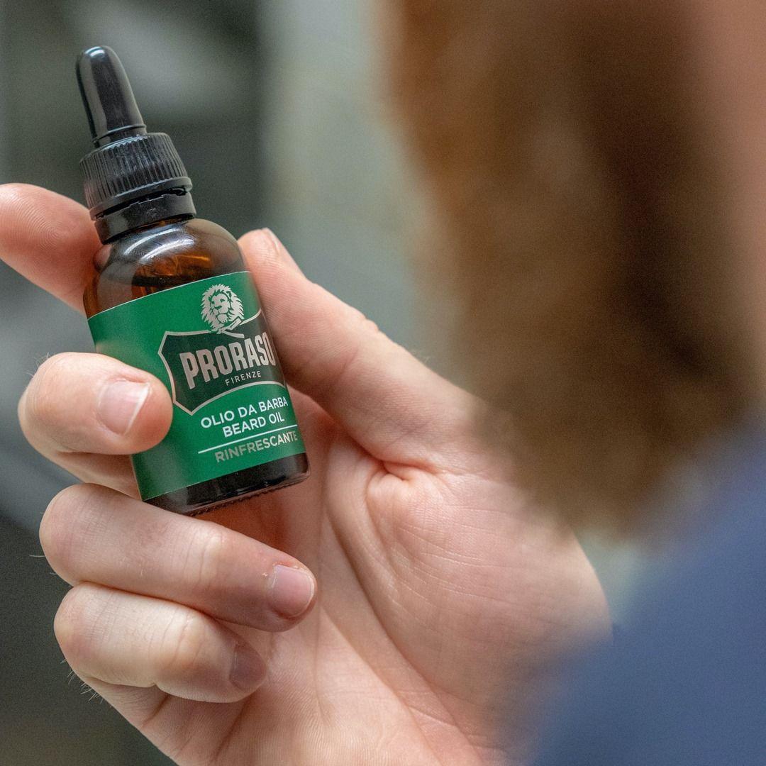 En man som håller i en liten flaska Proraso Refresh Beard Oil.